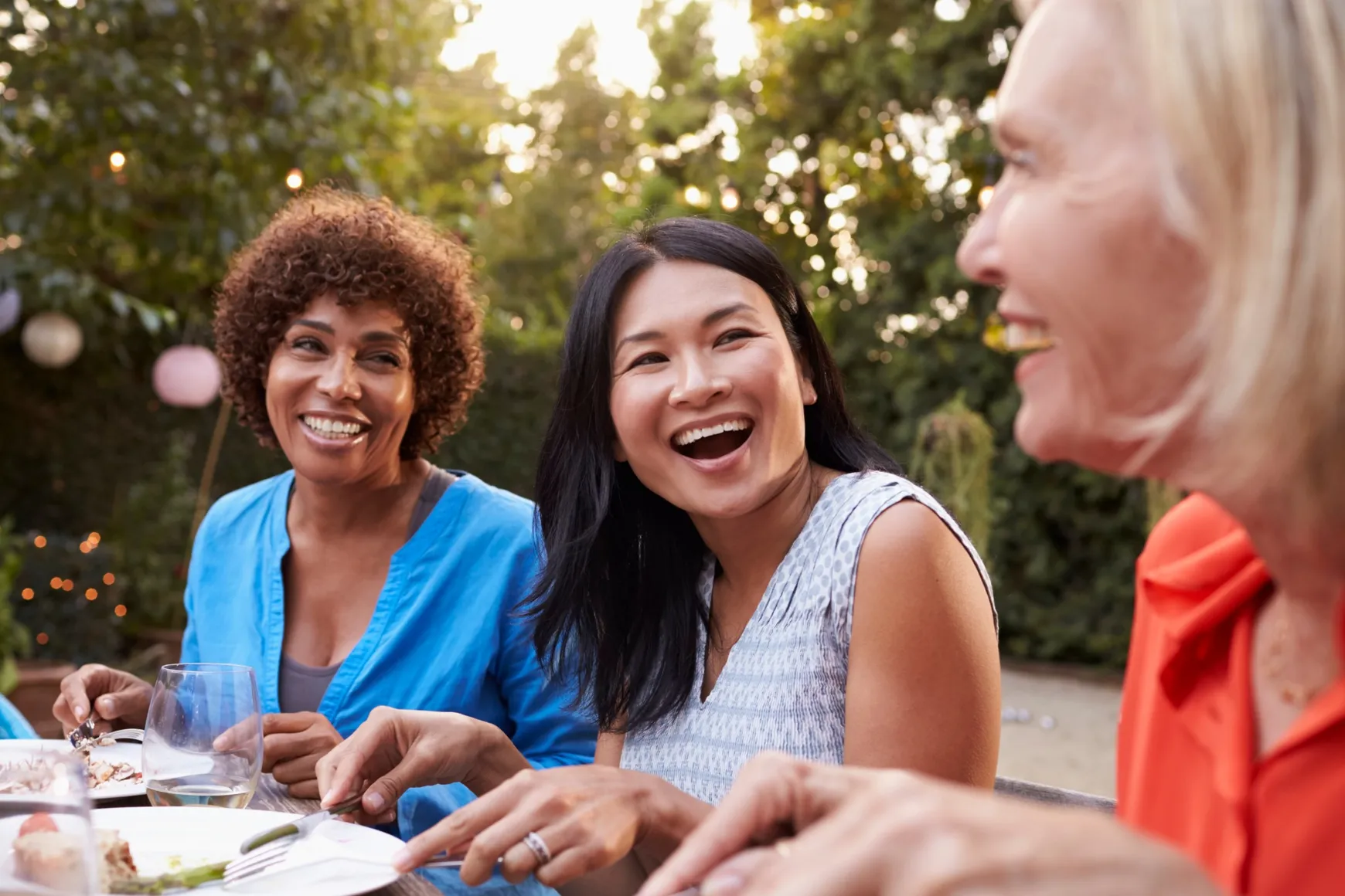 Three women smiling and laughing during an outdoor dinner with friends